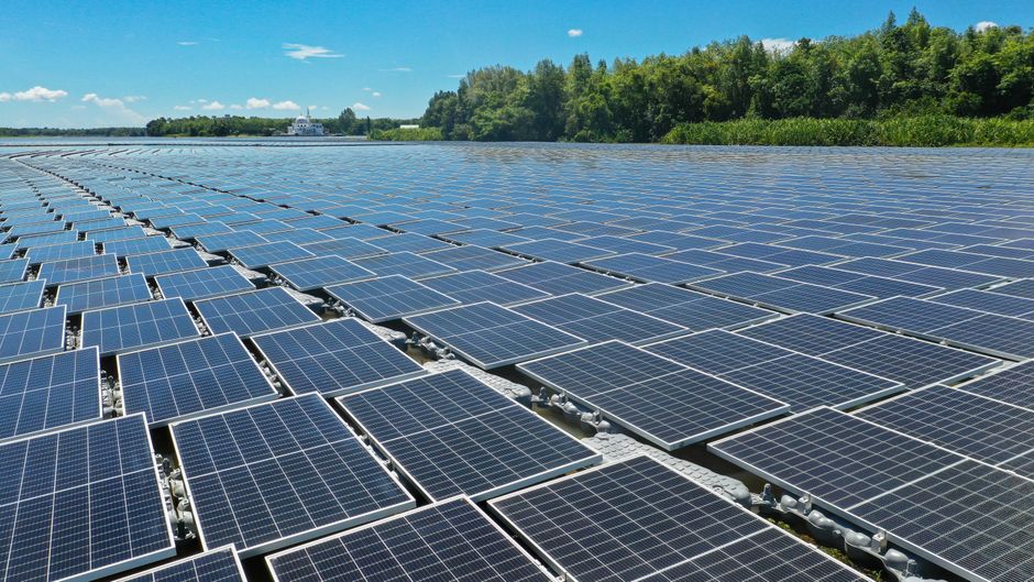 A large array of floating solar panels on a tranquil water surface with lush trees in the background.