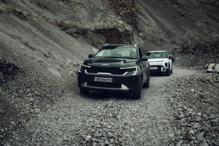 Kia SUVs driving through a rugged, rocky mountain pass in Ladakh, India.