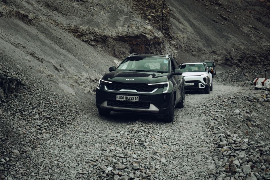 Kia SUVs driving through a rugged, rocky mountain pass in Ladakh, India.