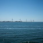 Wide view of an offshore wind farm against a clear blue sky and calm sea.