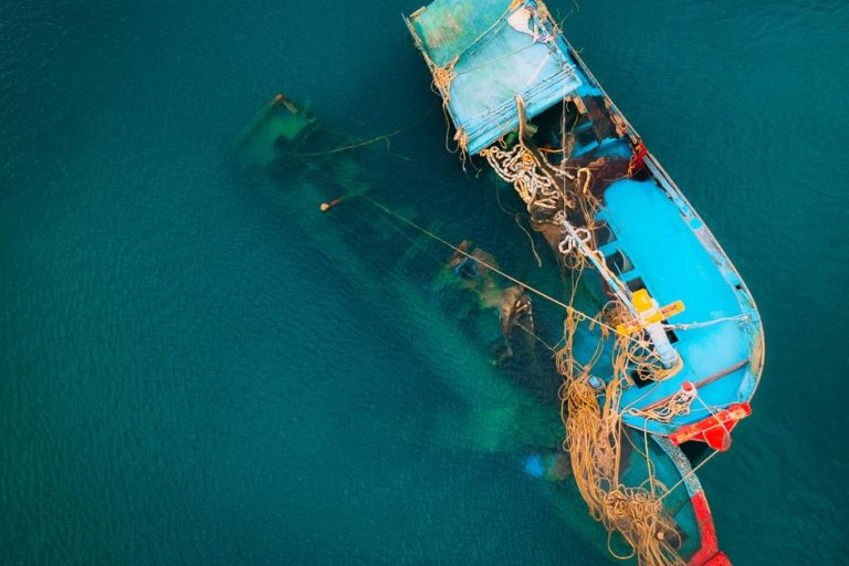 Aerial shot of a blue fishing boat partly submerged in clear ocean waters.