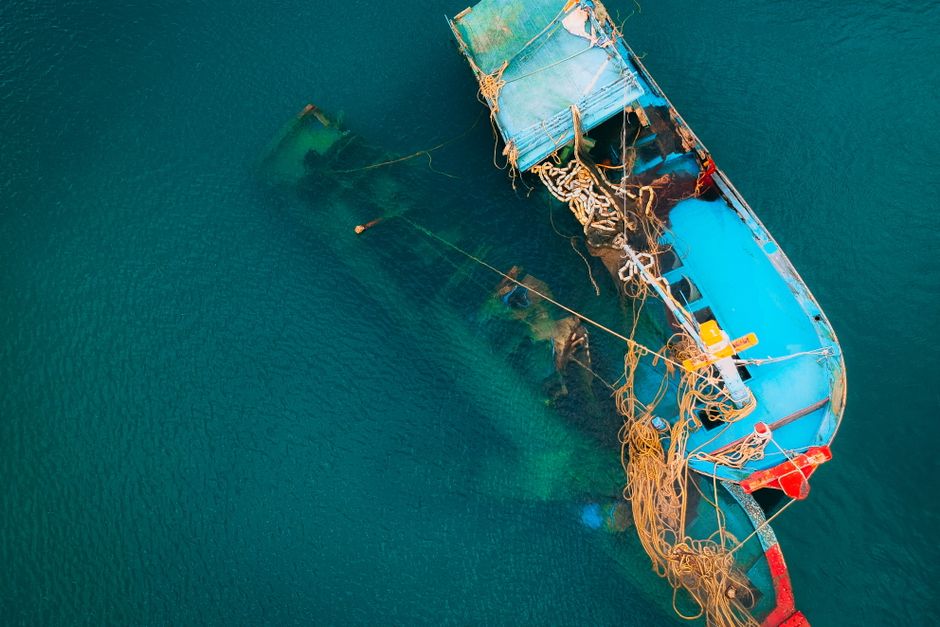 Aerial shot of a blue fishing boat partly submerged in clear ocean waters.