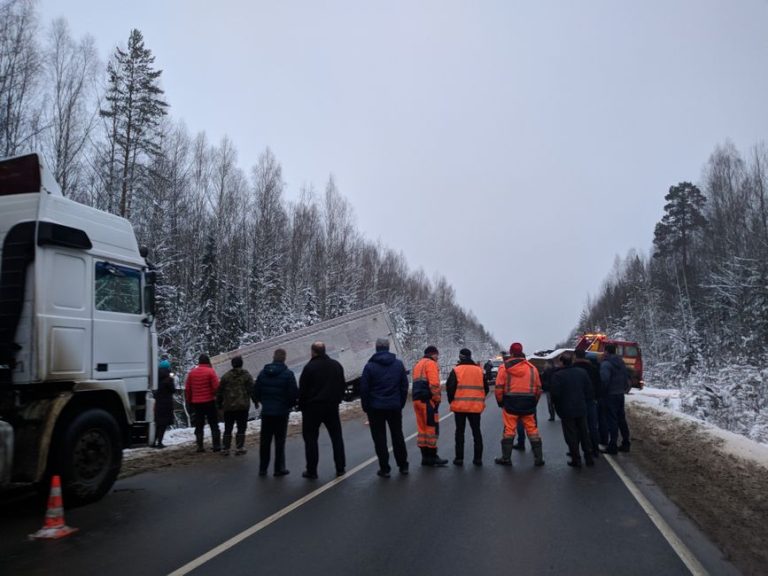 A group of people gather around a truck accident on a snowy Russian road.