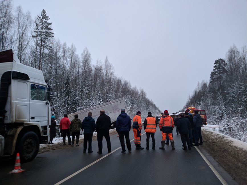 A group of people gather around a truck accident on a snowy Russian road.