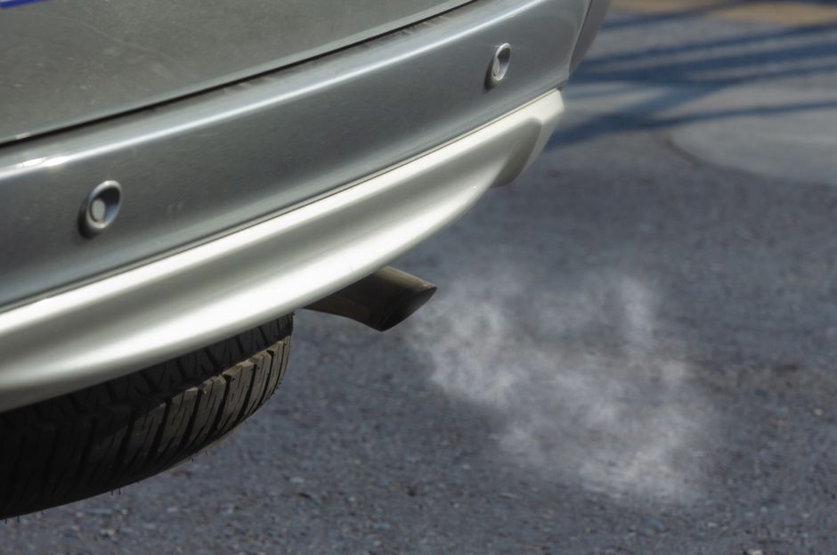 Close-up of a silver car exhaust pipe emitting smoke on asphalt road.