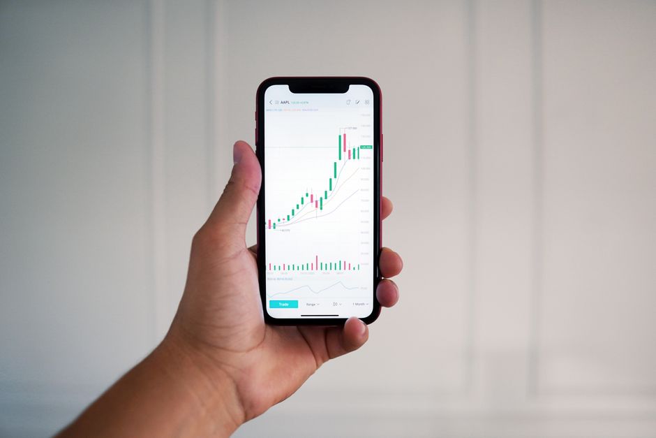 Close-up of a hand holding a smartphone showing a stock market chart indoors.