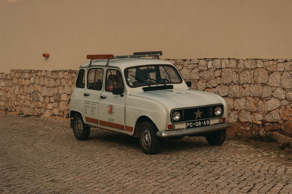 Classic white Renault parked on cobblestone street against a stone wall, exuding vintage charm.