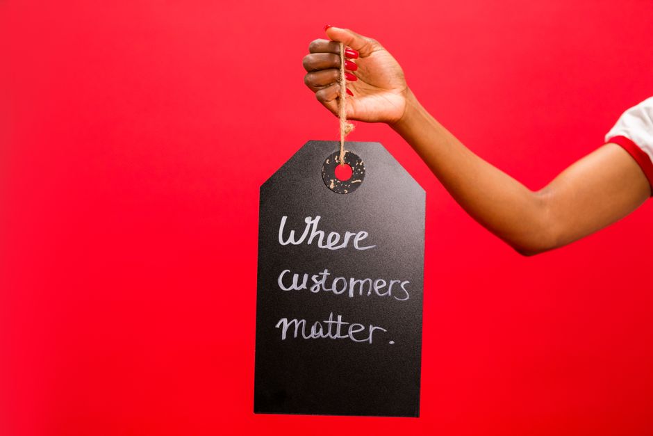 A hand holding a tag with 'Where customers matter' text on a vivid red background, emphasizing customer service.