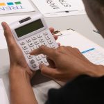 Focused image of a person using a calculator amidst financial documents and charts.