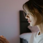 Profile of a young woman attentively using her smartphone indoors, lit by screen light.