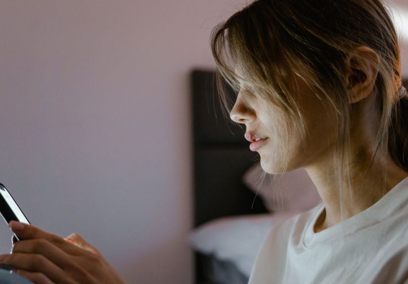 Profile of a young woman attentively using her smartphone indoors, lit by screen light.