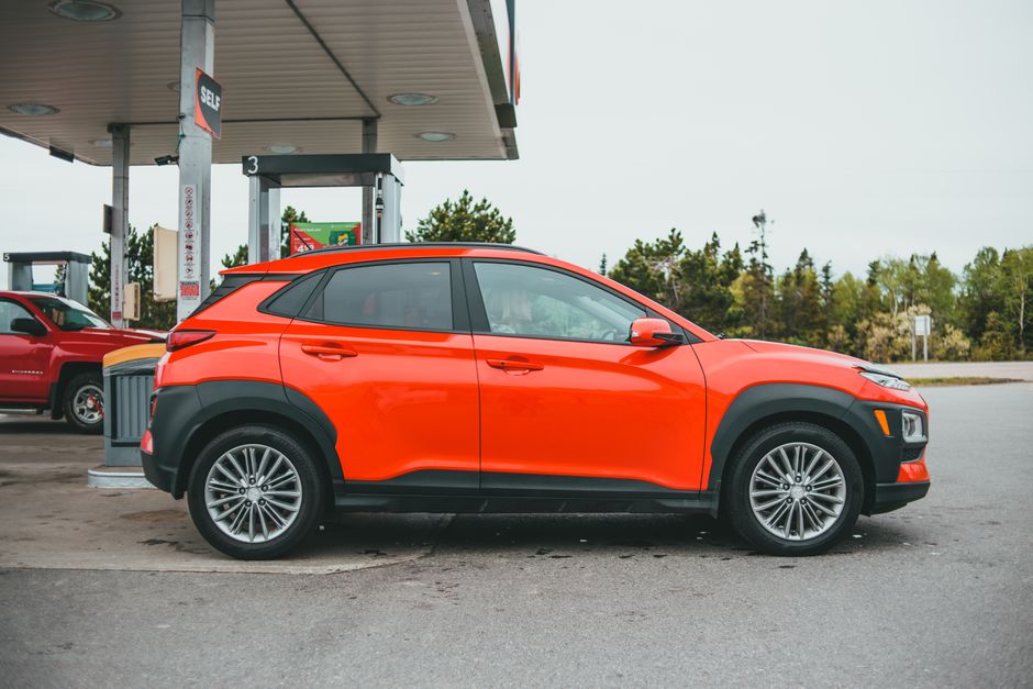 Bright orange SUV parked at a gasoline station with a red truck in the background.