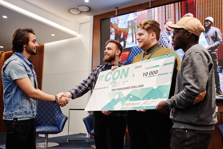 A group of men celebrating a win and receiving a large cheque at an IT conference.