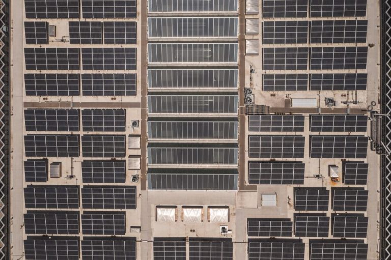 A high-angle drone shot capturing a grid of solar panels on a large industrial rooftop, showcasing renewable energy.