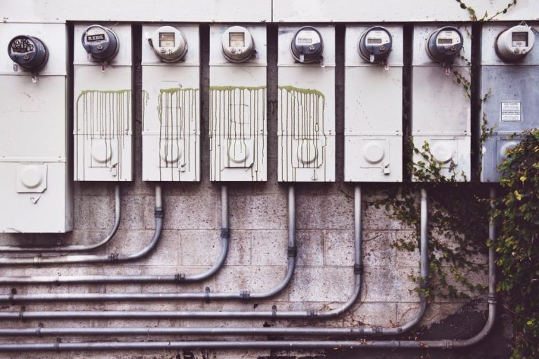 Array of outdoor electric meters on a brick wall with vines.