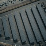 An aerial view showcasing a solar farm with aligned solar panels next to a busy parking lot.